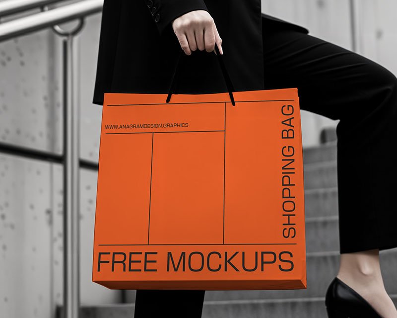 A woman in a black suit and heels holds an orange shopping bag labeled "FREE MOCKUPS" while walking up stairs