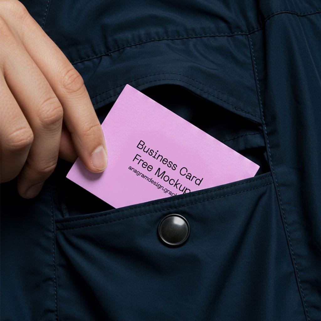 A hand sliding a pink business card mockup into the front pocket of a dark blue coat.