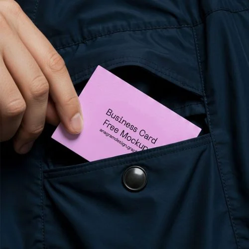 A hand sliding a pink business card mockup into the front pocket of a dark blue coat.